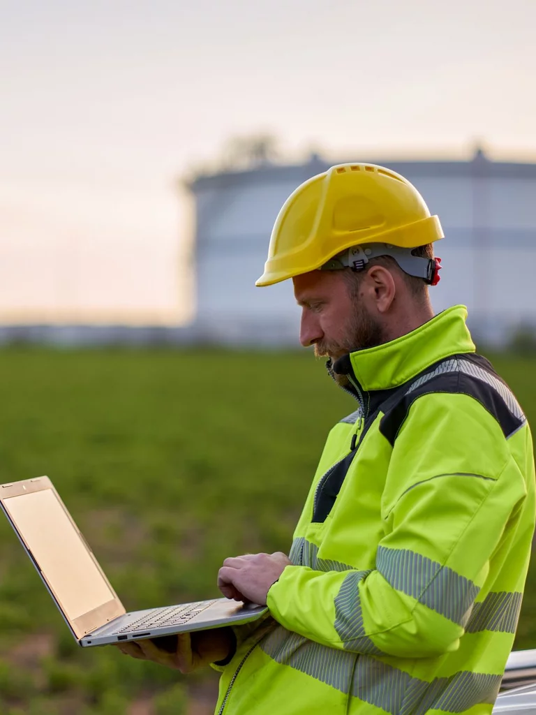 „Ein Mann in Sicherheitskleidung und gelbem Schutzhelm steht auf einem Feld und arbeitet mit einem Laptop